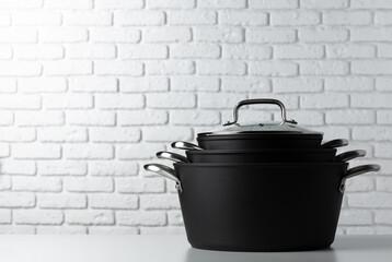 Black kitchenware on table against white brick wall