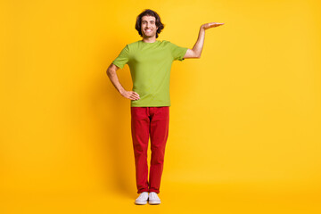 Full length body size photo of smiling man showing height wearing canvas shoes red pants green t-shirt isolated vivid yellow color background