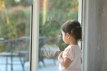 Sad asian little girl looking outside through the window