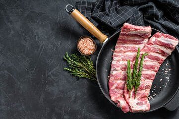 Raw pork spare ribs with spices and herbs in a pan. Black background. Top view. Copy space
