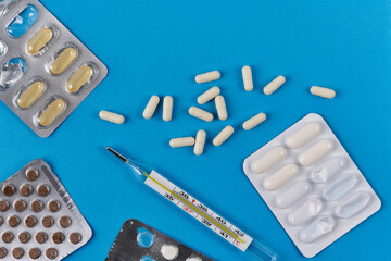 Mercury thermometer, white capsules and pills in packaging on a blue background