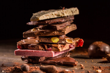 Stack of assorted chocolate with cocoa and cocoa beans on black background