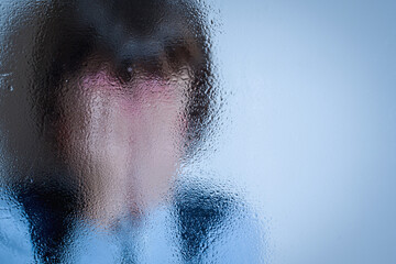 Children's fear and anxiety, psychological violence and pain. Little chidn girl covered her face with palms and cries behind wet glass. Selective focus. Copy space for text or design.