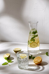 drink, detox and diet concept - glasses with fruit water or lemonade, lemons, limes and peppermint on white table