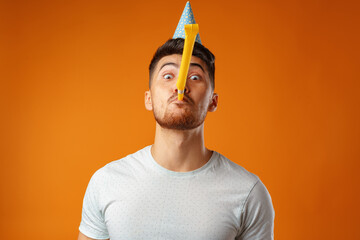 Happy man with party cone blowing into party horn