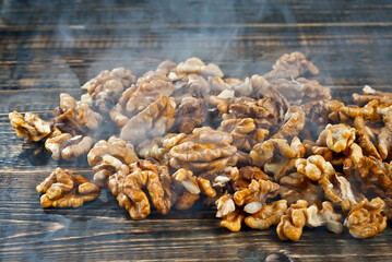 Walnut texture with steam close up. Many halves of peeled nuts on an old wooden board. Food in blue smoke on a background of shabby brown board.