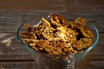 Peeled walnuts in a bowl. Nuts close up on an old wooden board. Food on a shabby table. Contrasting dramatic light as an artistic effect.