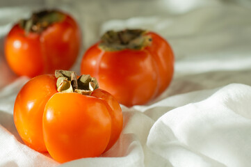 Persimmons lie on a white cloth and are illuminated by a single light source.
