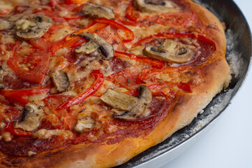 Cooked pizza with mushrooms, salami, cheese, peppers and tomatoes.