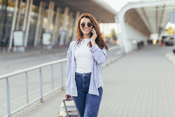 Young beautiful girl talking on the phone near a big bus stop with a suitcase