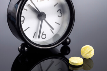 Yellow pills next to a clock, conceptual image