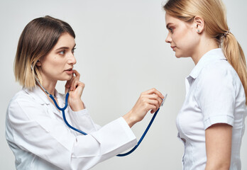 doctor with a stethoscope examines a woman in a white t-shirt on a light background