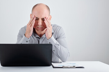 Portrait of stressed and tired middle-aged businessman sitting at desk in office and suffering from migraine after long day of work