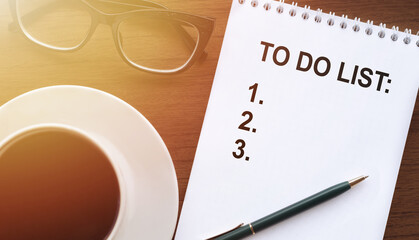 To do list - text on paper with cup of coffee and glasses on wooden background in sinlight.