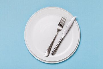 Empty white plate and cutlery on a blue background, top view. Food background