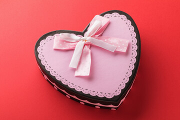Closed gift box with a heart-shaped bow on a red background, close-up