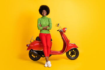 Obraz na płótnie Canvas Photo portrait of young girl driver on red scooter with crossed hands isolated on vivid yellow colored background