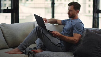 Beard man working remotely home. Male person sitting on couch with computer.