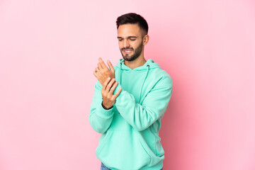 Young caucasian man isolated on pink background suffering from pain in hands