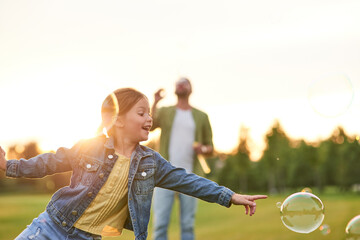 Adorable little girl having fun with soap bubbles on a sunny day, daughter and dad spending time...