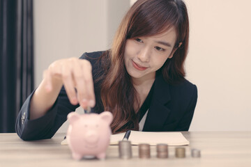 Obraz na płótnie Canvas An Asian woman is putting coins into a piggy bank to practice saving discipline for future use, money saving concept.