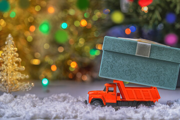 A toy red truck carries a festive box with a Christmas gift on a colorful sparkling bokeh background. The Concept Of Merry Christmas.