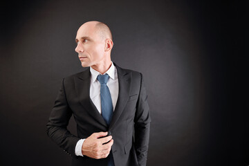 Handsome confident mature man in stylish suit looking away, isolated on dark background