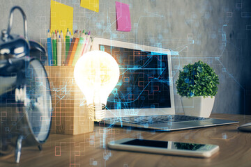 Computer on desktop in office with bulb icon hologram. Double exposure. Concept of idea.