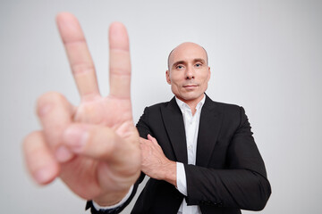 Confident mature entrepreneur or politician showing peace gesture and looking at camera, isolated on white