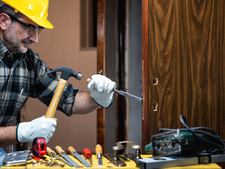 Close-up. Carpenter at work repairs and installs the new lock of a wooden door. Construction...