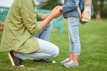 Cropped shot of young father holding daughter's hands, daddy spending time with his little girl in the green park on a warm day