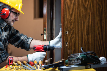 Close-up. Carpenter at work repairs and installs the new lock of a wooden door. Construction...
