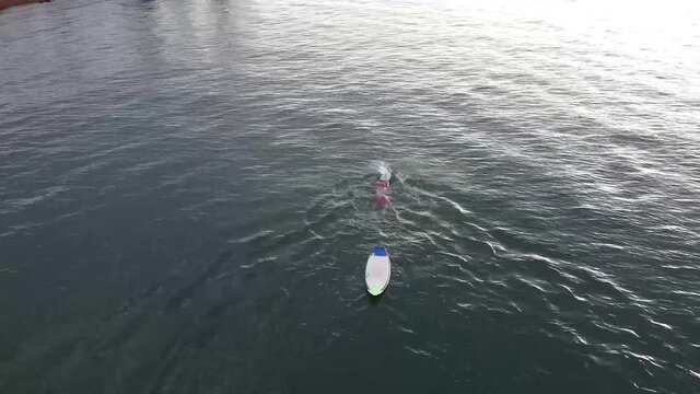 Homem nadando num lago arrastando sua prancha amarrada por uma corda