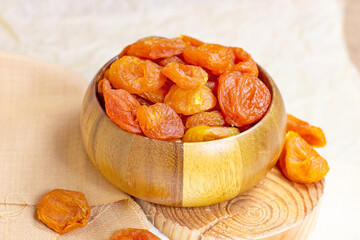 Orange dried apricots in wooden bowl on light background.