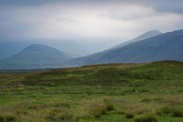 misty landscape of Iceland, a bright green field and mountains in the fog