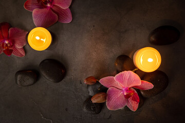 orchid flowers with spa stones and candles on dark rock background. beauty treatment and wellness concept. top view