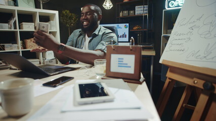 Fototapeta na wymiar Cheerful african businessman stacking money at modern workplace in slow motion.