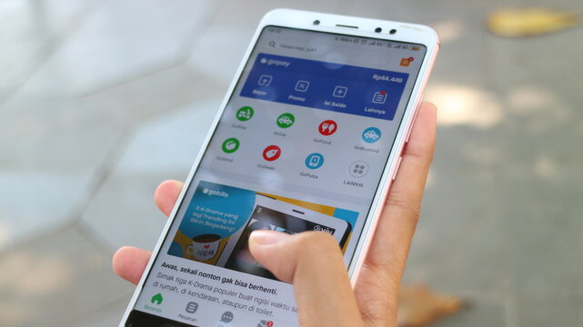 Display the Gojek application by hand and blur the background