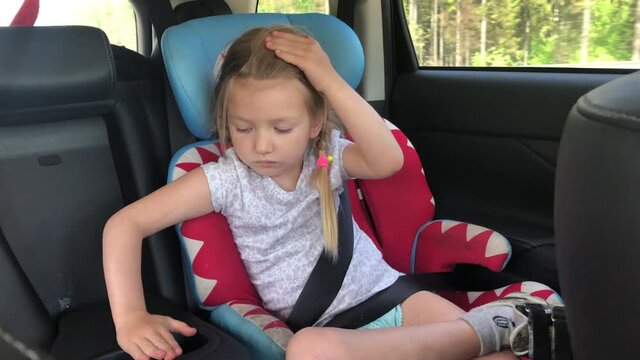 A little girl rides buckled in a car seat in a car in the summer.