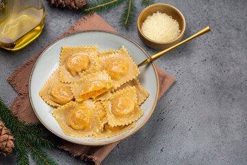 Italian  Christmas eve dinner: tortelli or ravioli stuffed with pumpkin and parmesan cheese. Grey table. Copy space. christmas decoration. Vertical image.
