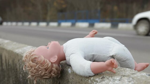 A baby doll lies on the side of a highway.Abandoned doll on the road.