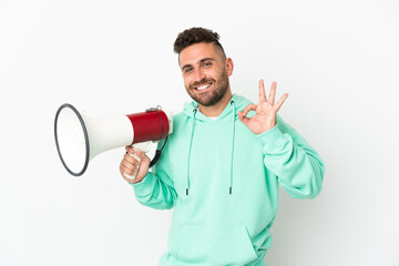 Caucasian man isolated on white background holding a megaphone and showing ok sign with fingers