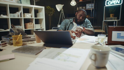 Portrait of african american guy working with papers near laptop in dark office.