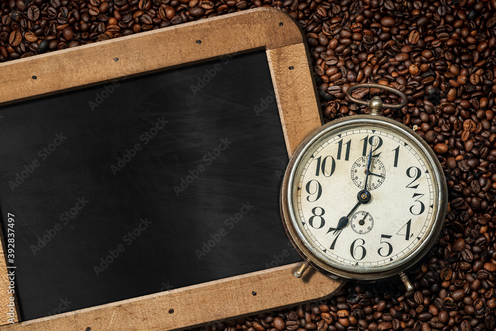 Poster closeup of an old alarm clock on background with many roasted coffee beans and empty blackboard with