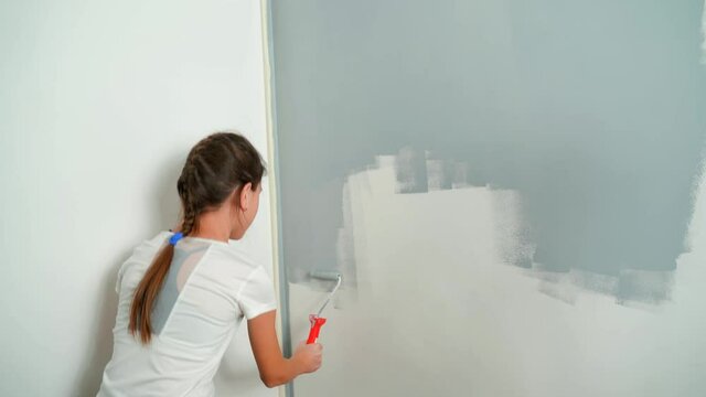 A young girl paints the wall with a roller gray. Room Renovations at Home.