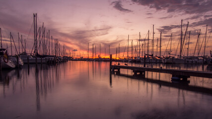 Silhouettes of sailing boats and piers in dutch harbour at dusk