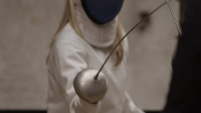 Close-up two fencers with swords woman in white and a man in black compete while in an old apartment. Concept of confrontation between good and evil. Slow motion
