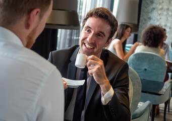 Colleagues and friends. Two cheerful businessmen drinking coffee and talking to each other