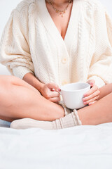 Comfortable woman at home holding a cup of coffee or tea with warm woolen clothes. Concept being at home