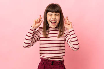 Little girl isolated on pink background with fingers crossing